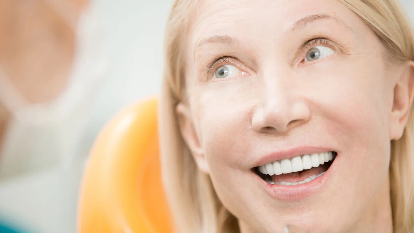Imagen de una mujer en su visita al dentista mientra sonríe feliz y mira con mirada cómplice a su dentista de confianza
